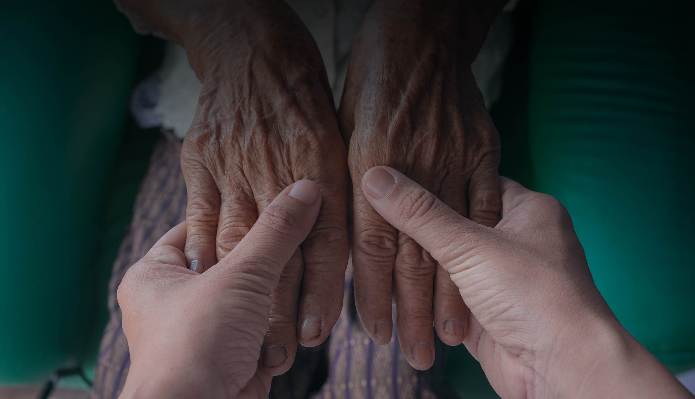 An elder's hands held gently in a caregiver's hands